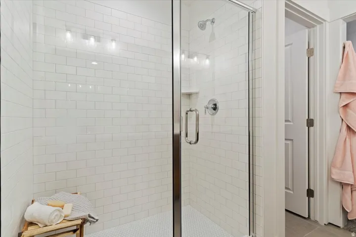 Shower enclosure with clear glass door, subway tile surround, hexagon tile flooring, built-in recessed shelf, and chrome fixtures