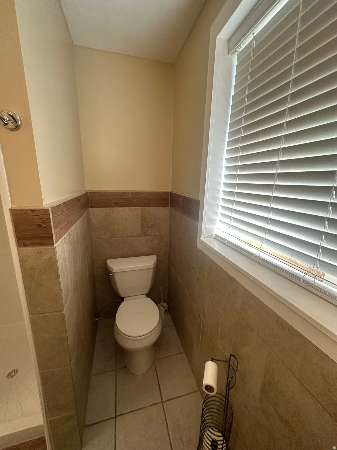 Tiled walls with wood-finish accent, tiled flooring, and a window with blinds