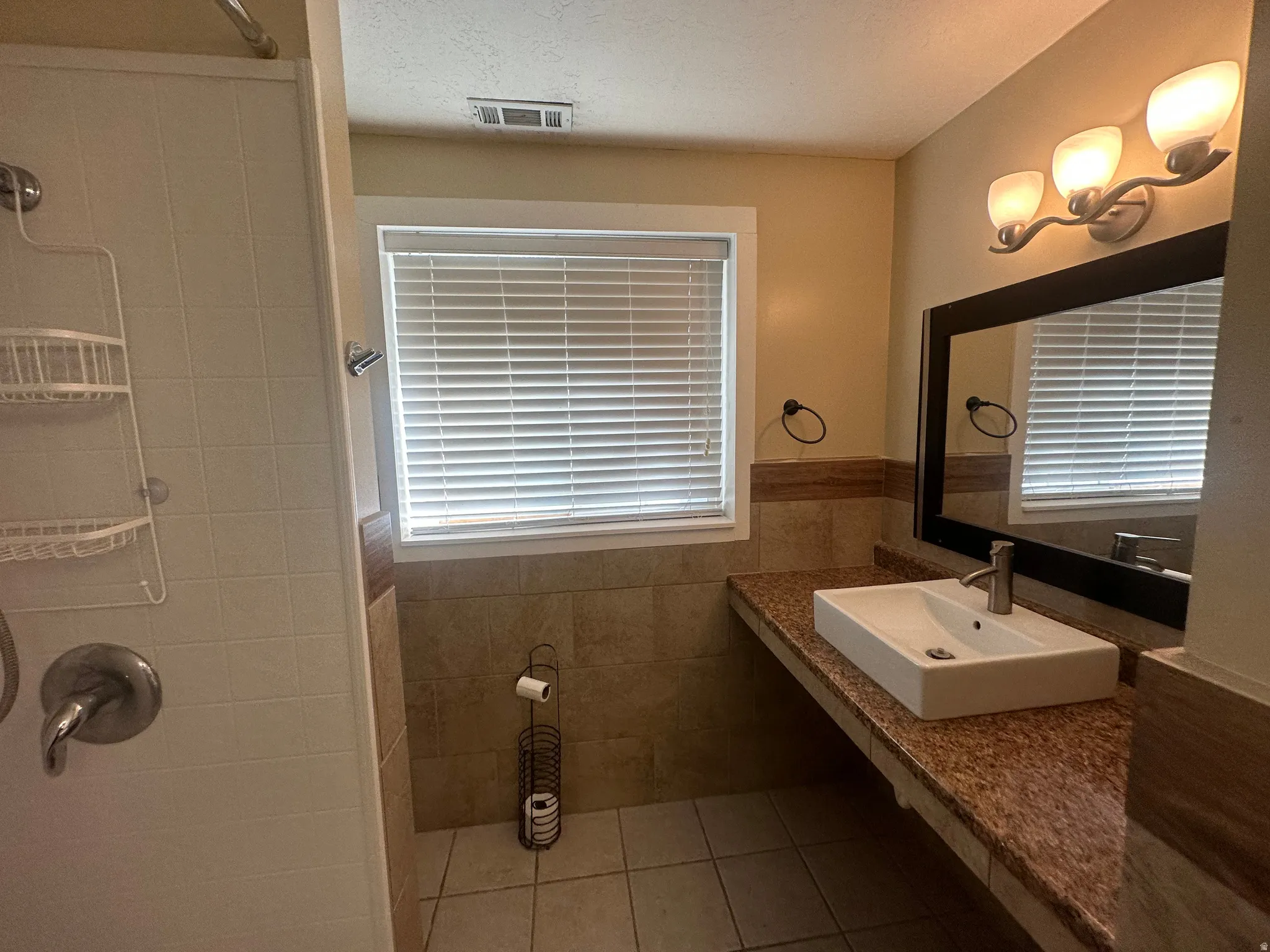 Integrated shower and tub combination, rectangular vessel sink, granite-finish countertop, framed wall mirror, and modern vanity lighting