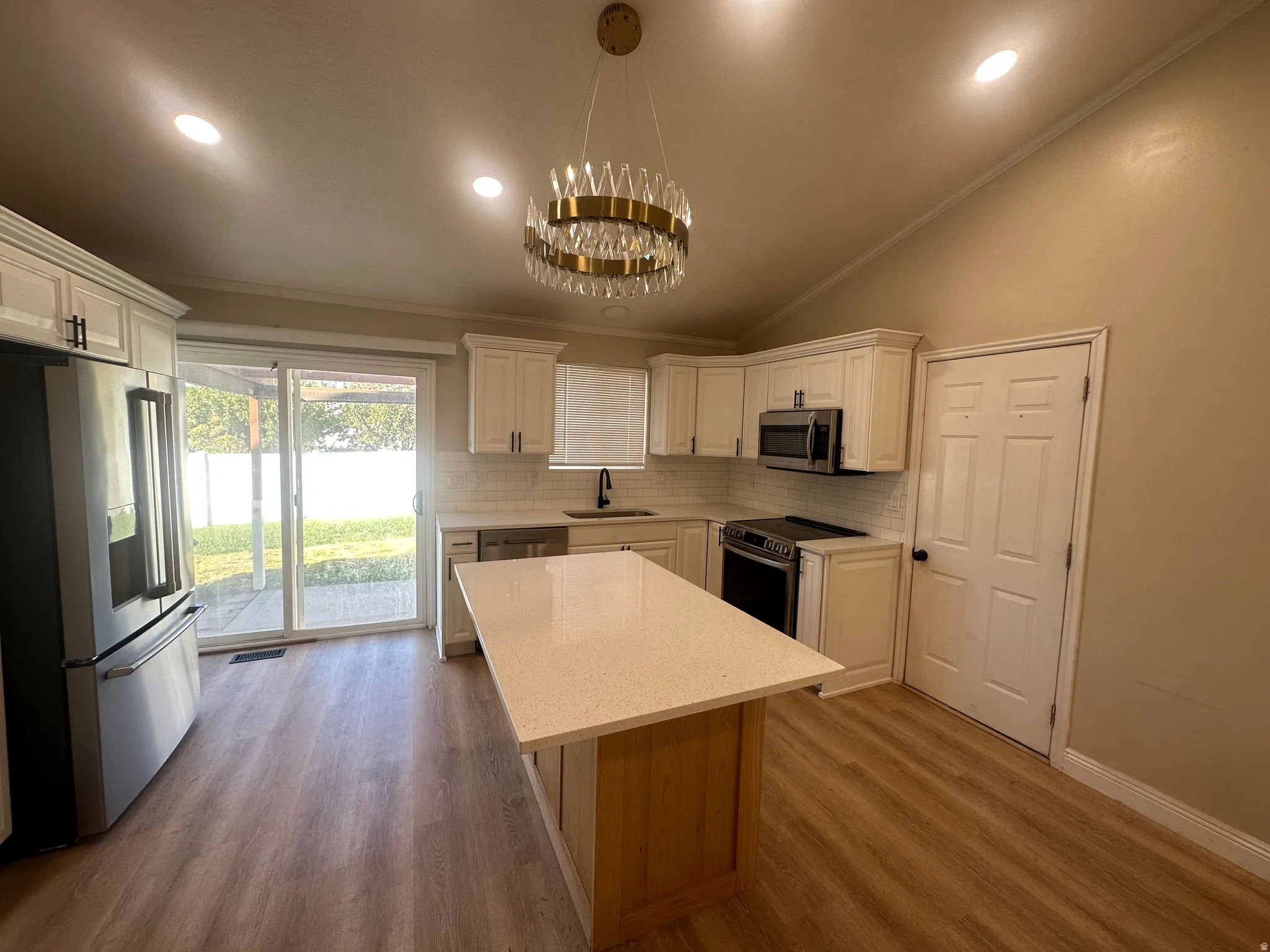 Vaulted ceiling with recessed lighting, white shaker cabinetry, stainless steel appliances, central island with light-toned countertop, and wood-finish flooring