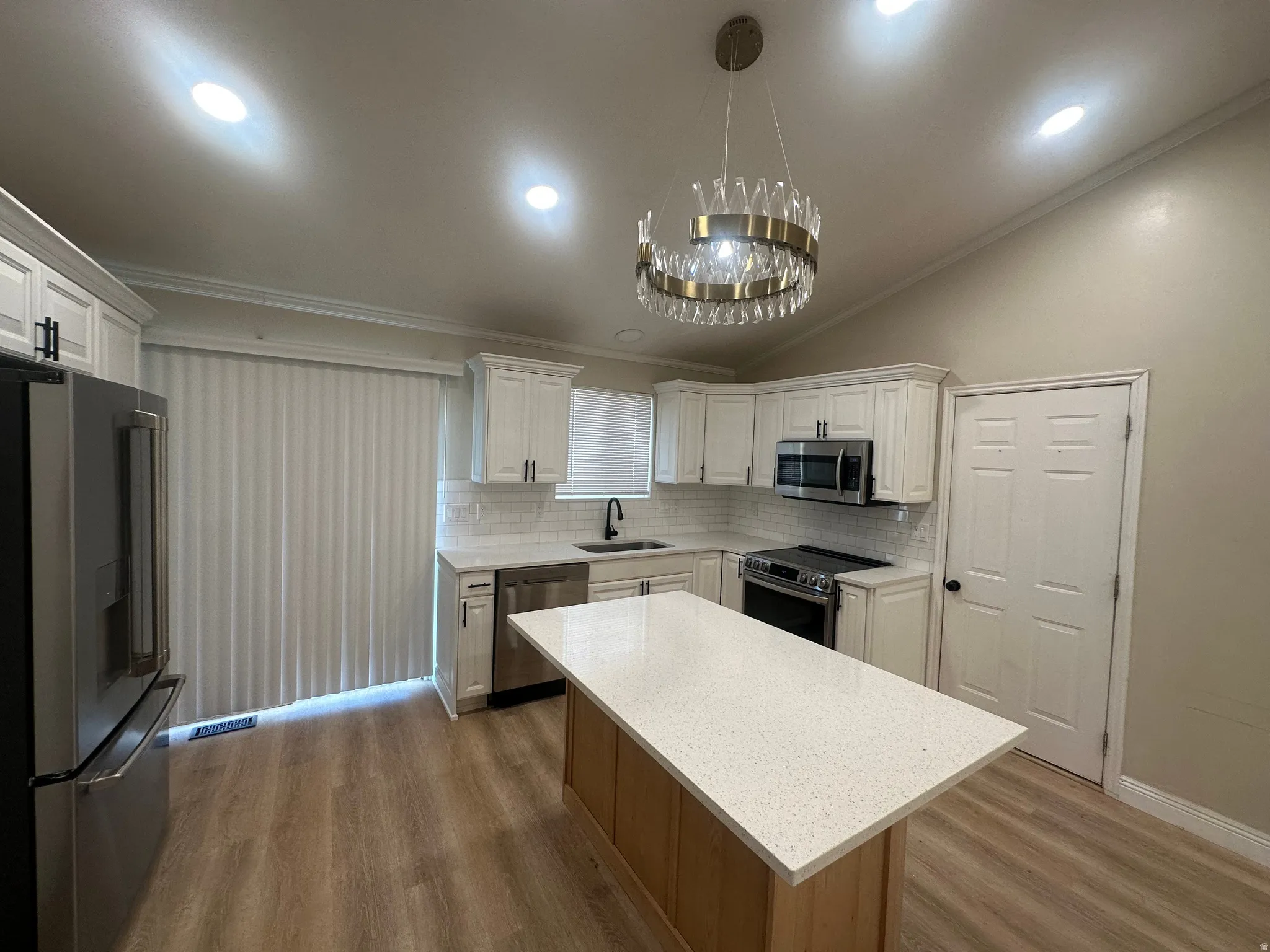 Kitchen featuring wood-finish flooring, white cabinetry, stainless steel appliances, and a central island with a light-toned countertop