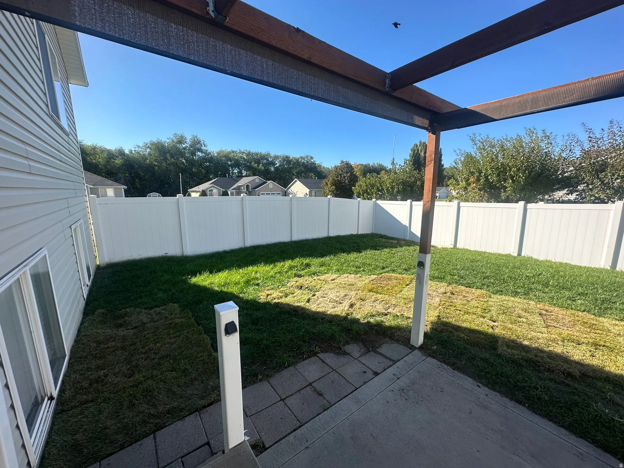 Patio area with concrete and paver sections, leading to a fenced backyard with established grass