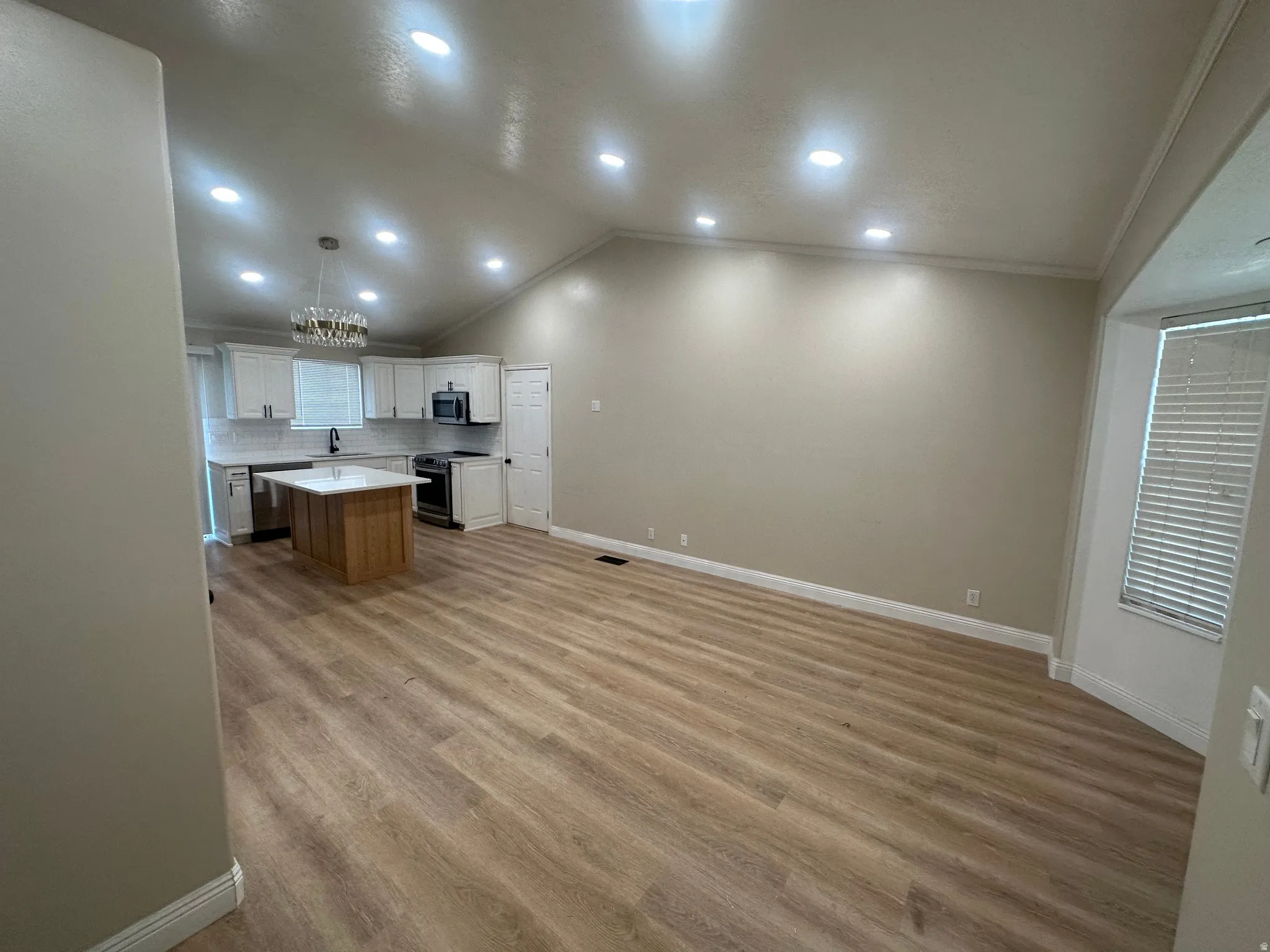 Open-concept living area featuring wood-finish flooring, vaulted ceilings, recessed lighting, and a modern kitchen with a central island and white cabinetry