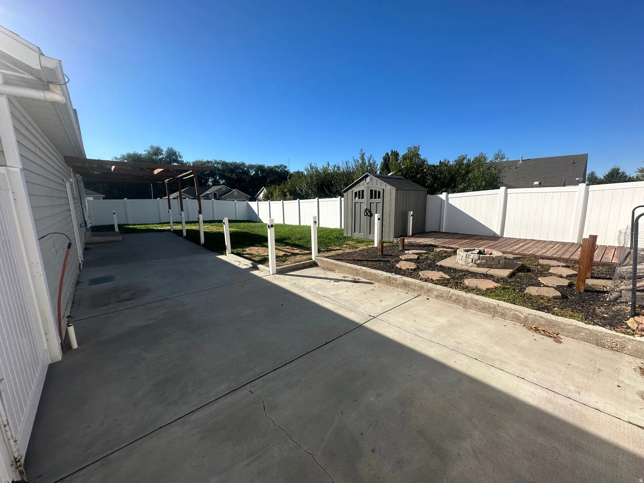 Concrete patio with a wood pergola, leading to a landscaped area featuring a fire pit, stepping stones, and a raised wood deck