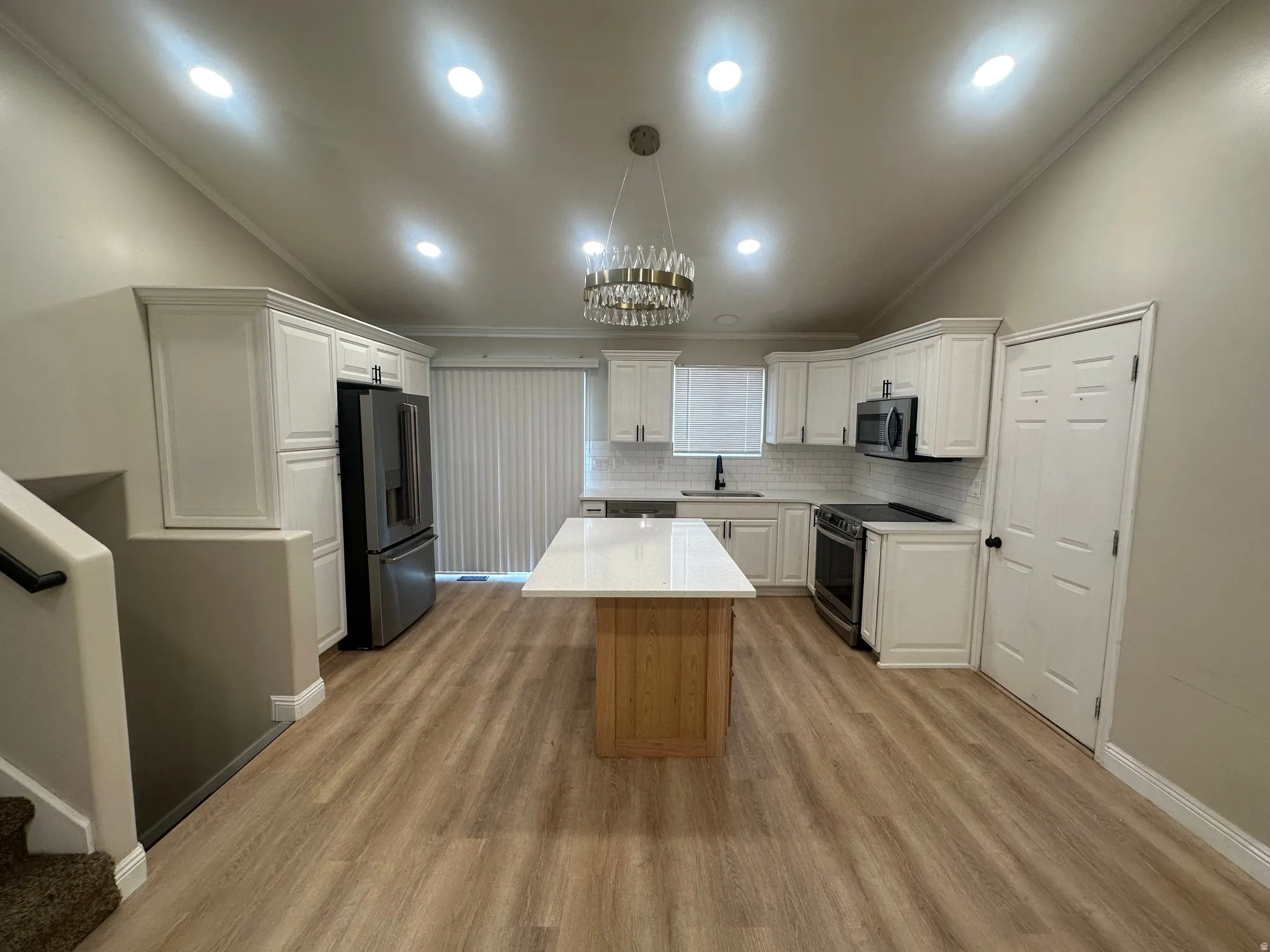 Vaulted ceiling, recessed lighting, wood-finish flooring, white cabinetry, and a central island with a solid surface countertop