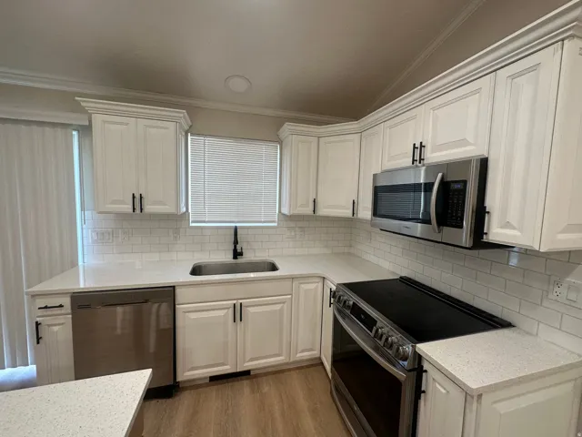White shaker cabinetry, stainless steel appliances, white subway tile backsplash, light-toned countertops, and wood-finish flooring