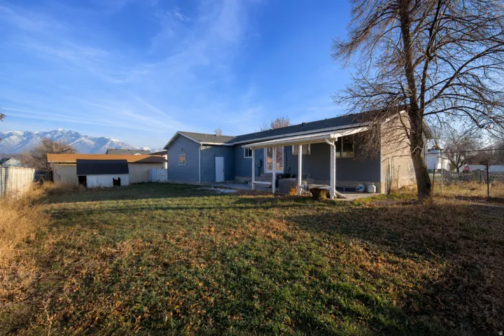 Expansive backyard with a covered patio, multiple storage sheds, and a chain-link fence