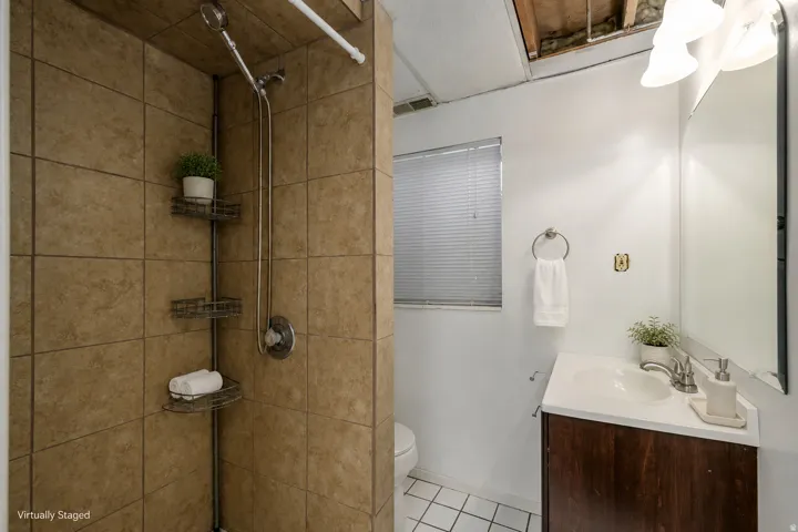 Shower with large format tile surround, chrome fixtures, and corner shelving unit