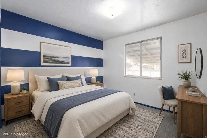 Master bedroom featuring bold navy and white horizontal striped accent wall, wood-finish nightstands with integrated task lighting, queen-size bed with layered bedding in coordinating navy and cream tones, large windows with natural light, wood-finish dre