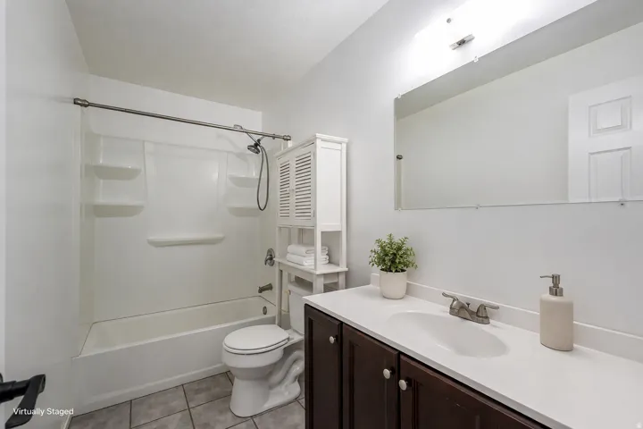 Tub and shower combination with built-in shelving, dark wood-finish vanity with white countertop, and wall-mounted mirror