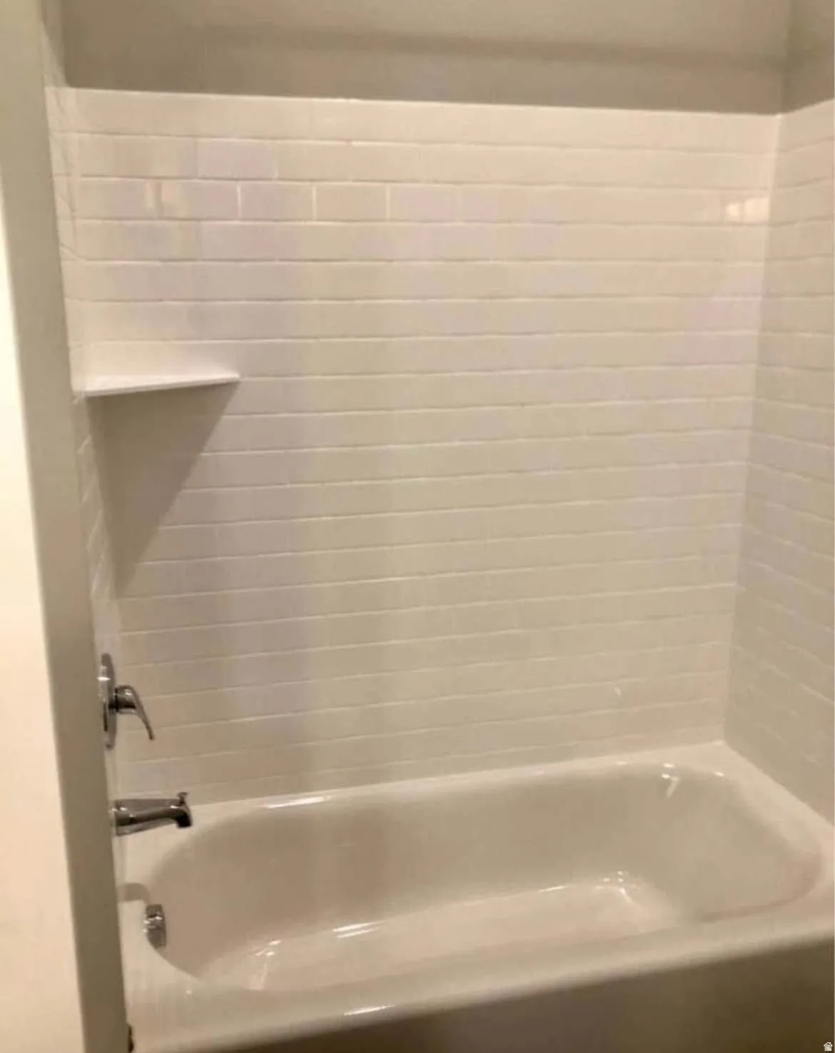 White subway tile surround with integrated shelf, built-in bathtub, and chrome fixtures