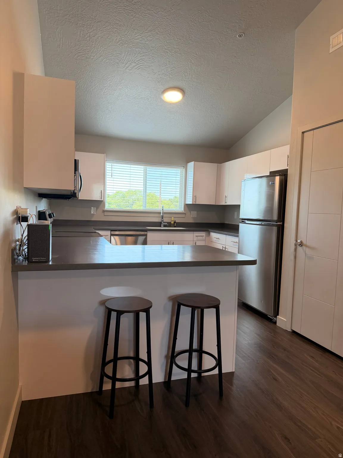 Kitchen featuring white cabinetry, stainless steel appliances, dark countertops, a breakfast bar, and wood-finish flooring