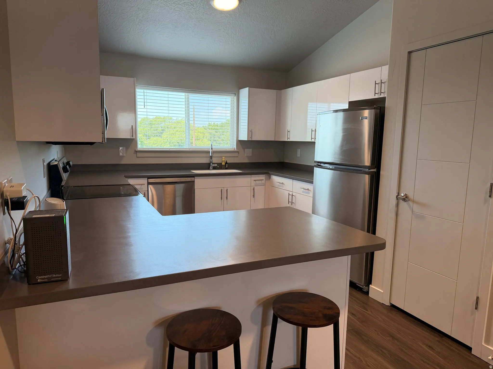 Contemporary kitchen featuring white cabinetry, stainless steel appliances, a breakfast bar, and wood-finish flooring