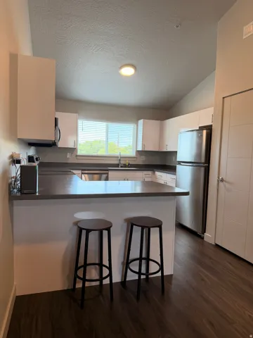 Kitchen featuring white cabinetry, stainless steel appliances, dark countertops, a breakfast bar, and wood-finish flooring