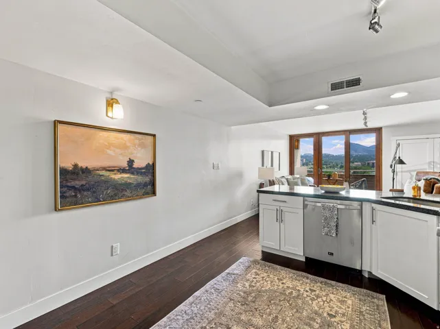 Dark wood-finish flooring, white cabinetry with dark countertops, stainless steel dishwasher, track lighting, and sliding glass doors