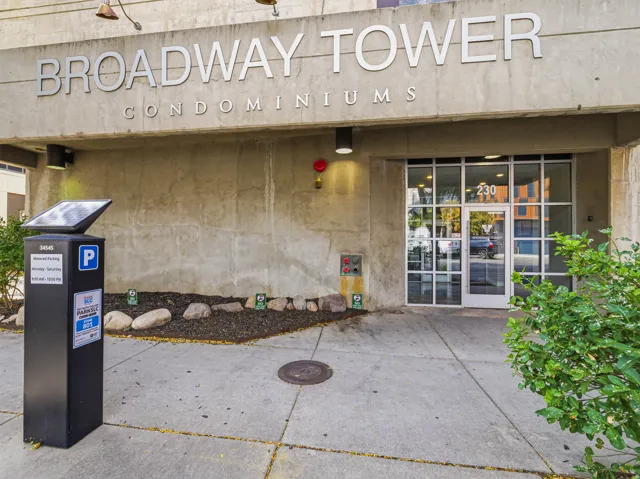 Concrete facade with prominent building signage, glass-paneled entrance door, and integrated exterior lighting