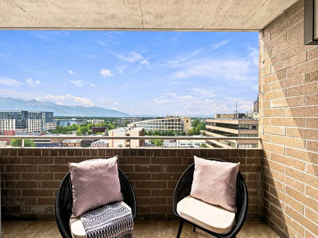 Balcony with durable brick walls, a concrete ceiling, and a metal railing overlooking a cityscape with mountain scenery
