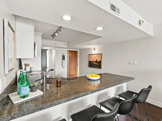 Kitchen island with granite countertop, integrated sink, and white cabinetry