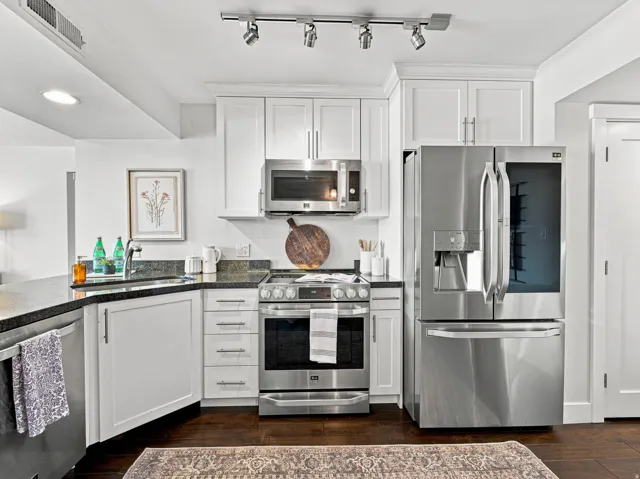 Modern kitchen featuring white cabinetry, stainless steel appliances including a dual-oven range and French-door refrigerator, black granite countertops, and track lighting