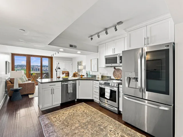 Open-concept kitchen featuring white cabinetry, stainless steel appliances, dark countertops, and wood-finish flooring
