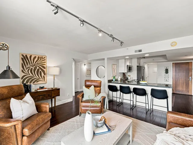 Dark wood-finish flooring complements the modern kitchen with white cabinetry and a breakfast bar