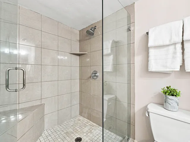 Glass-enclosed shower with full-height tile surround, built-in tile bench, and integrated corner shelf
