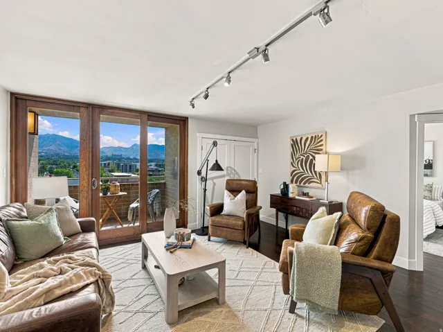 Sophisticated living room showcasing panoramic mountain vistas through expansive wood-frame glass doors, neutral wood-finish flooring, and track lighting
