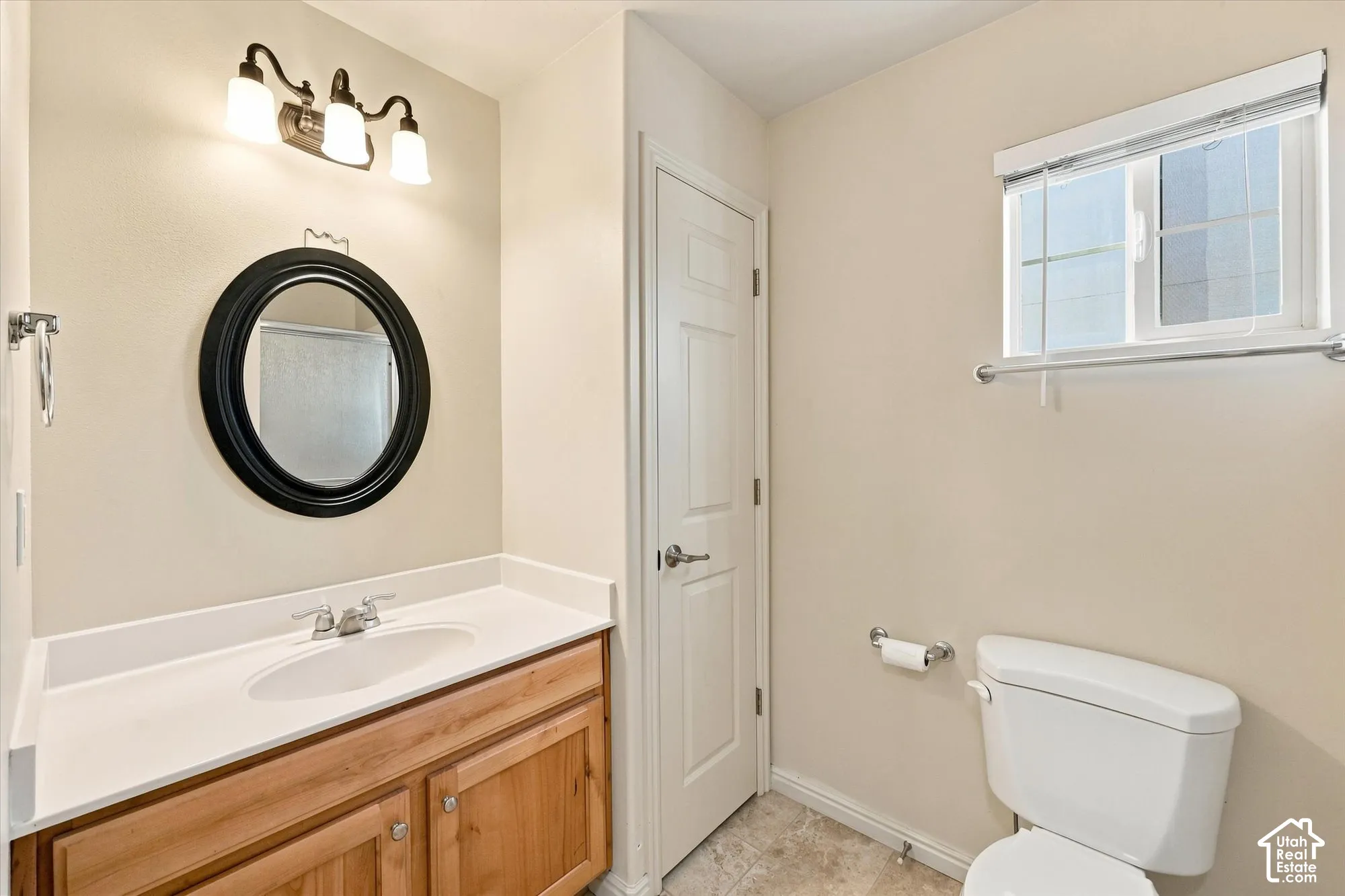 Wood-finish vanity with a white countertop and integrated sink, complemented by a round black-framed mirror