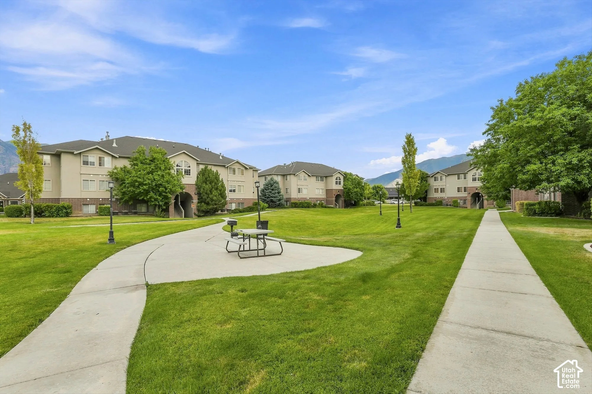 Expansive green space featuring paved walkways, mature trees, and exterior lighting fixtures