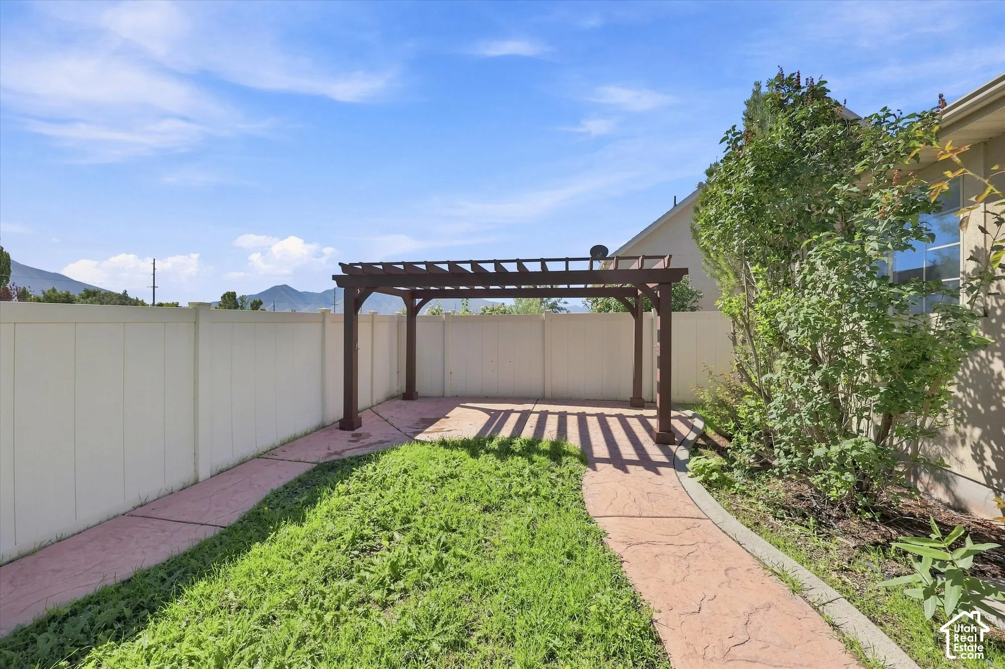Backyard featuring a wooden pergola, concrete pathway, and perimeter fencing