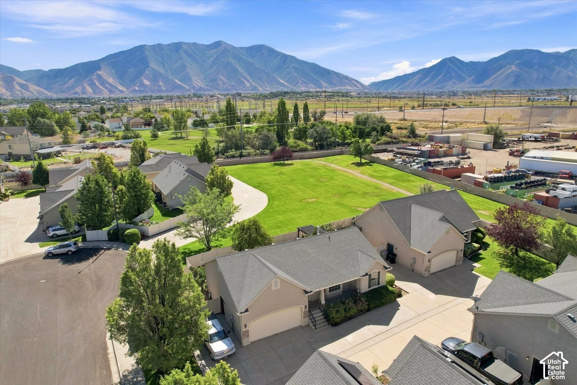 Property featuring a light-colored exterior, an attached garage, a paved driveway, and a shingled roof, all set against a distant mountain range