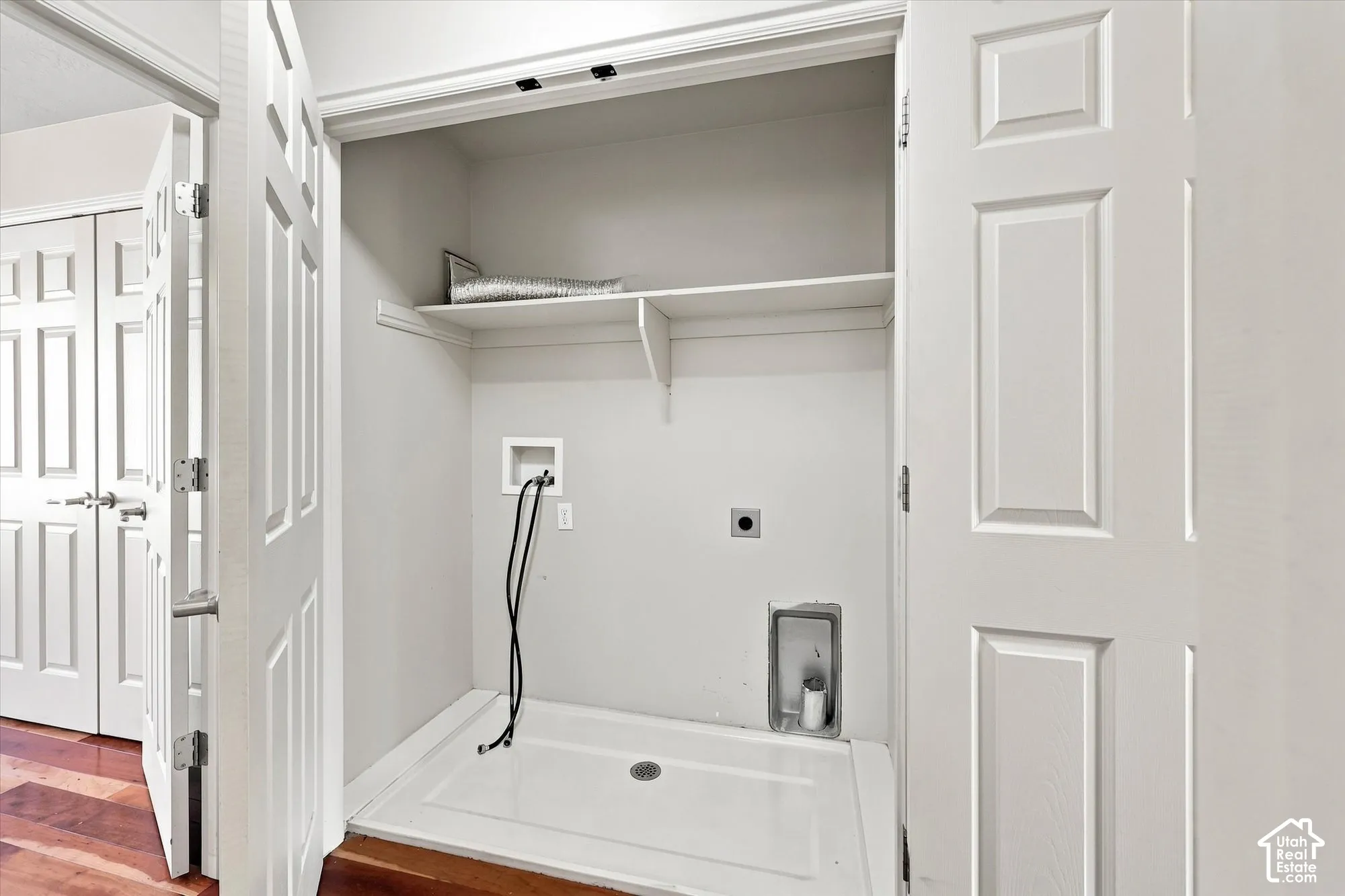 Utility closet with a white laundry pan and integrated shelf storage