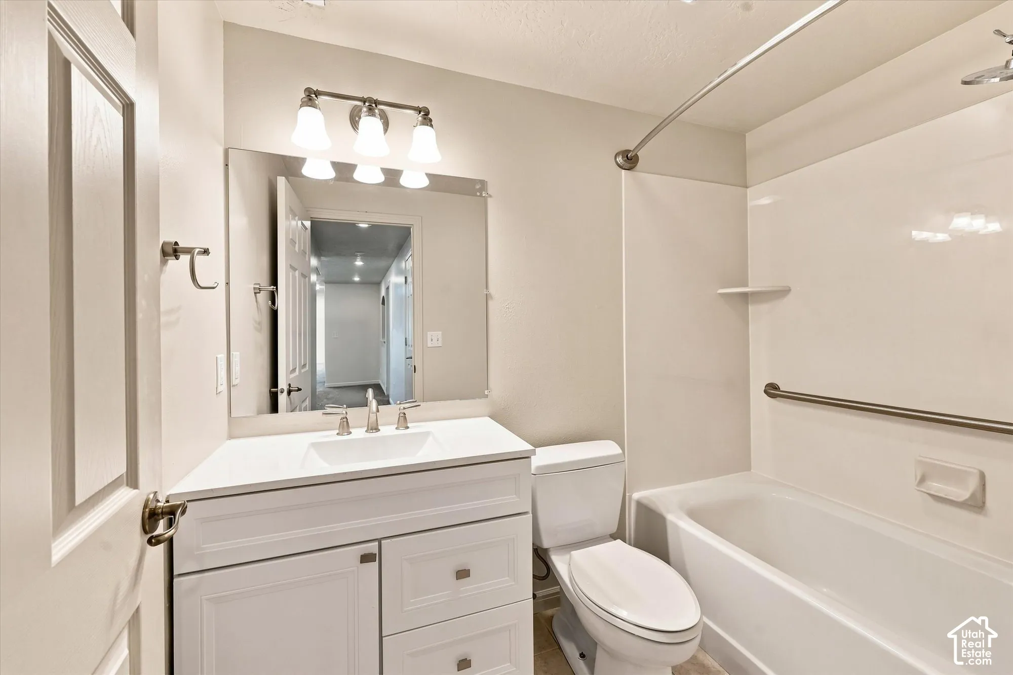 White vanity with integrated sink, three-light vanity fixture, large wall-mounted mirror, and a full-size bathtub with shower combination