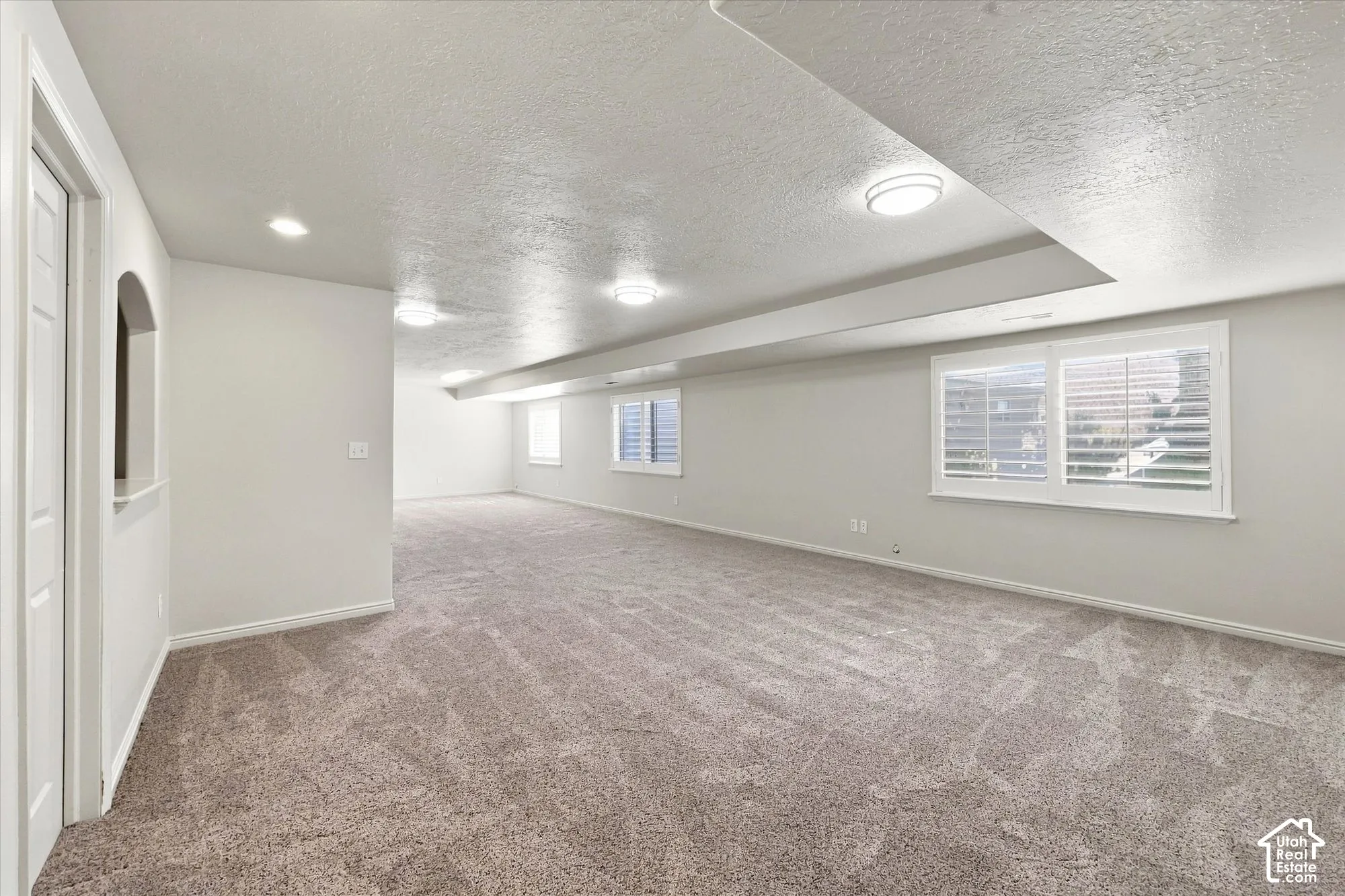 Spacious room featuring neutral carpeting and multiple windows with plantation shutters