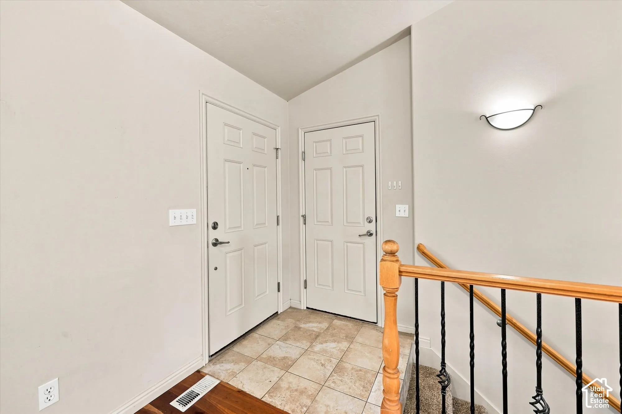Tiled entryway with two paneled doors, hardwood-finish flooring, and a decorative wall sconce