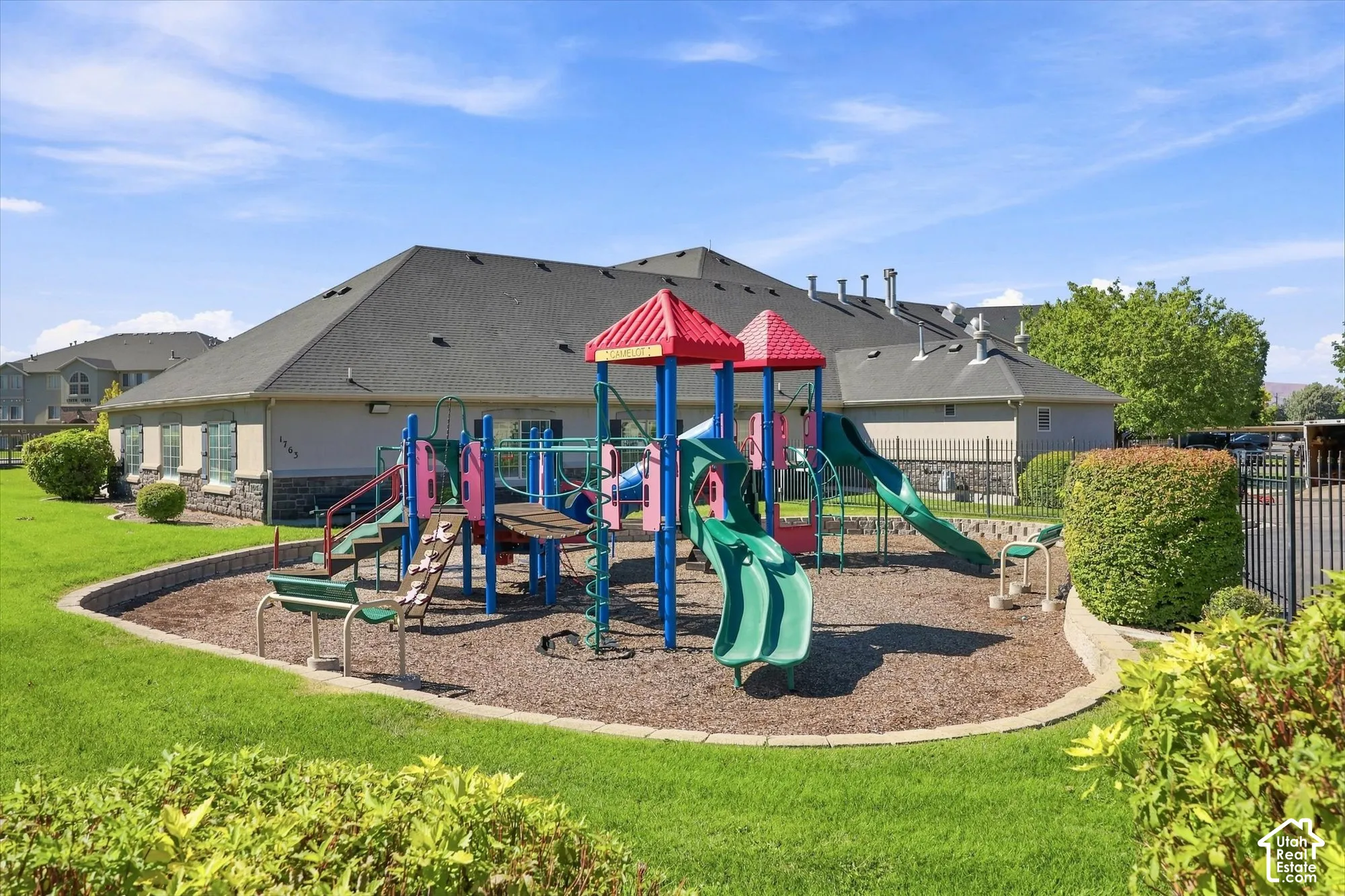 Recreational playground structure with multiple slides and climbing features, surrounded by woodchip surfacing and a retaining wall