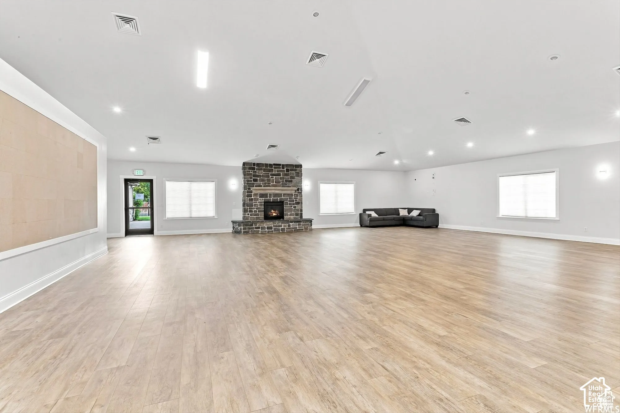 Spacious room featuring wood-finish flooring, a stone fireplace, recessed lighting, multiple windows, and a built-in wall panel