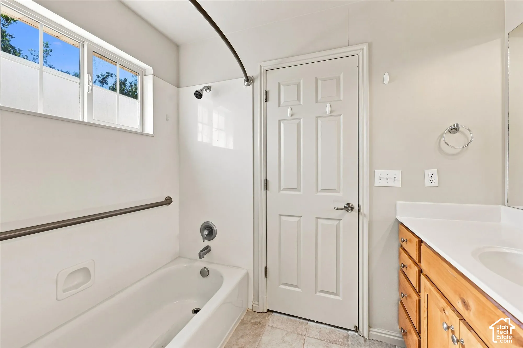 White bathtub with shower, horizontal window, wood-finish vanity with white countertop, and neutral wall paint