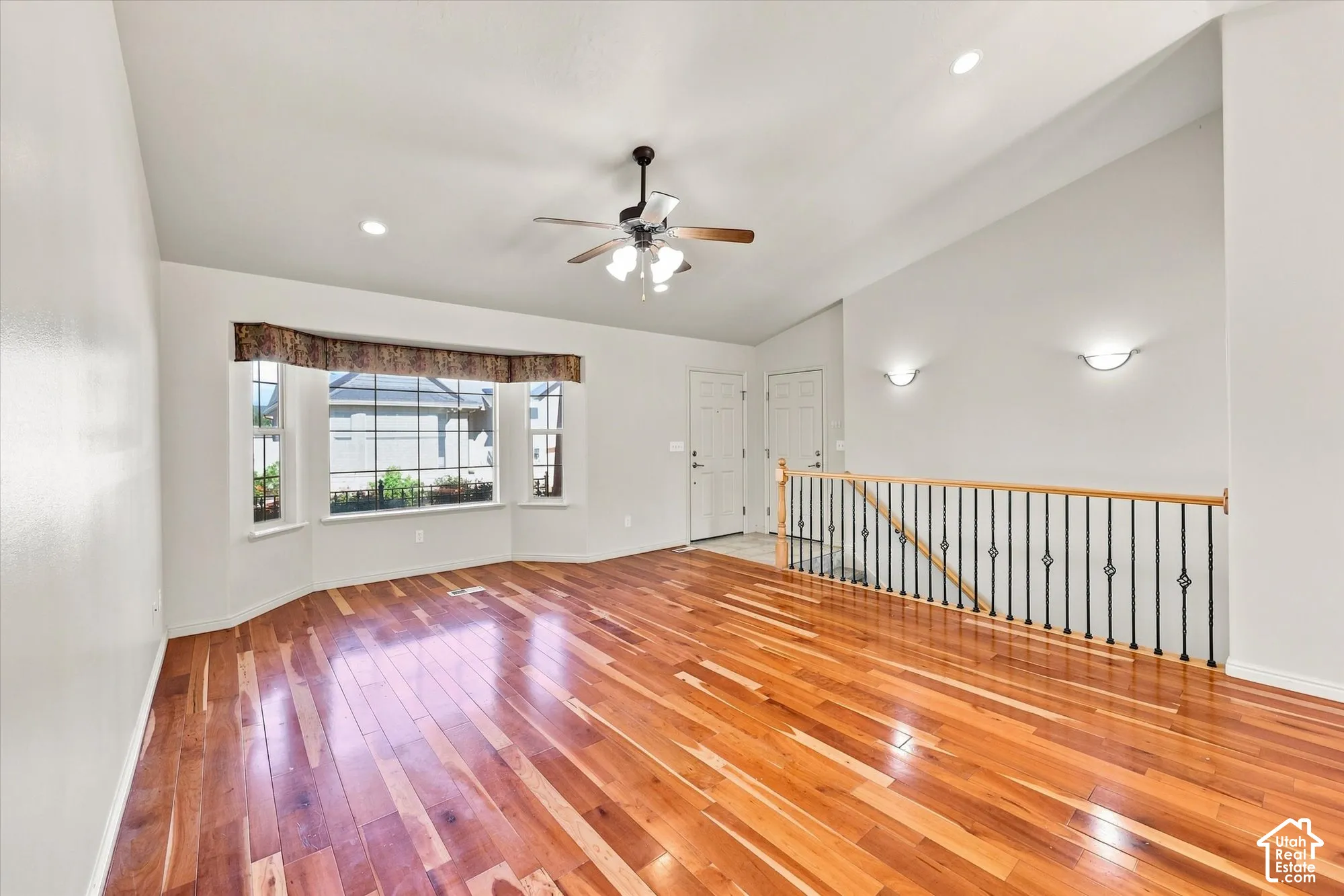 Hardwood flooring, bay window, vaulted ceiling, ceiling fan, and wrought iron railing
