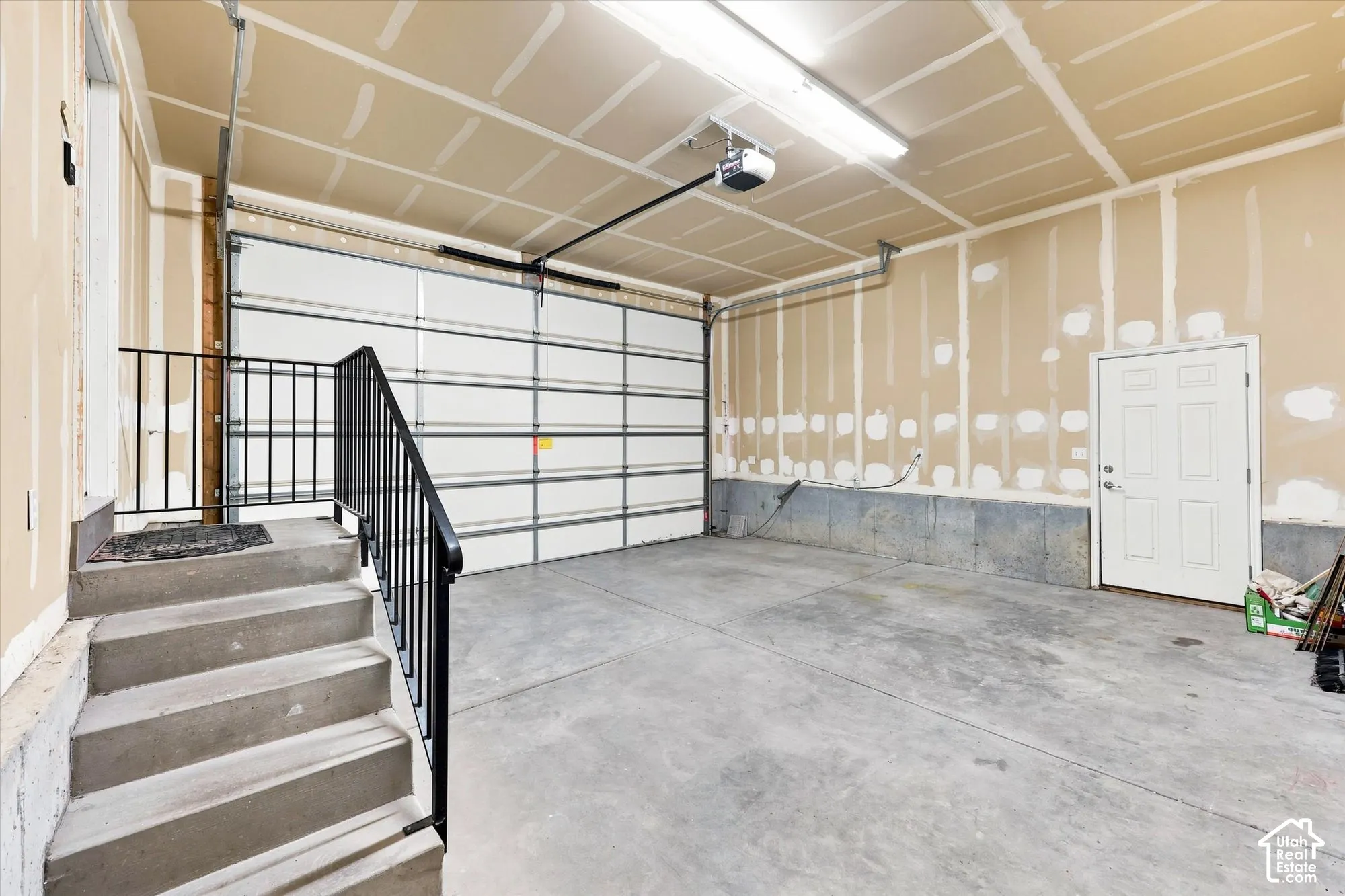 Garage with concrete flooring, automatic overhead door, and concrete stairs with black metal railing