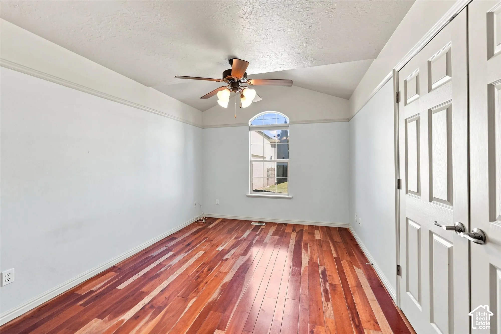 Vaulted ceiling with a ceiling fan, arched window, wood-finish flooring, and panel doors