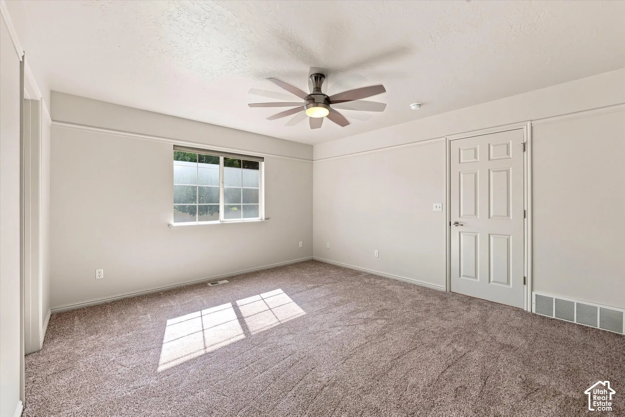 Neutral wall paint, textured carpet flooring, ceiling fan with integrated lighting, white trim work, and a six-panel interior door