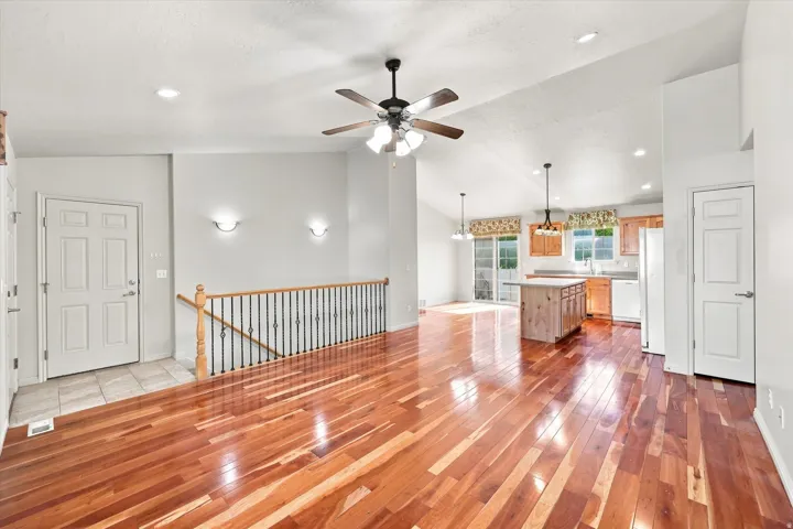 Wood-finish flooring throughout, vaulted ceiling, recessed lighting, ceiling fan with integrated lighting, and an open-concept kitchen with a central island