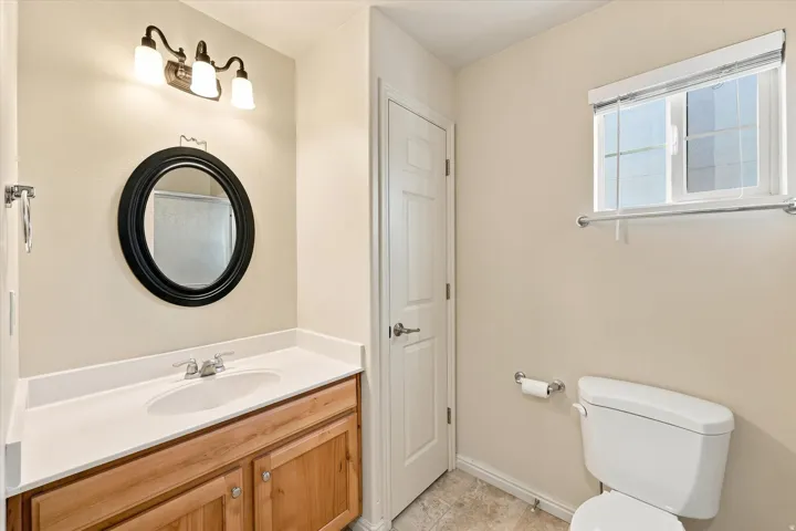 Wood-finish vanity with a white countertop and integrated sink, complemented by a round black-framed mirror