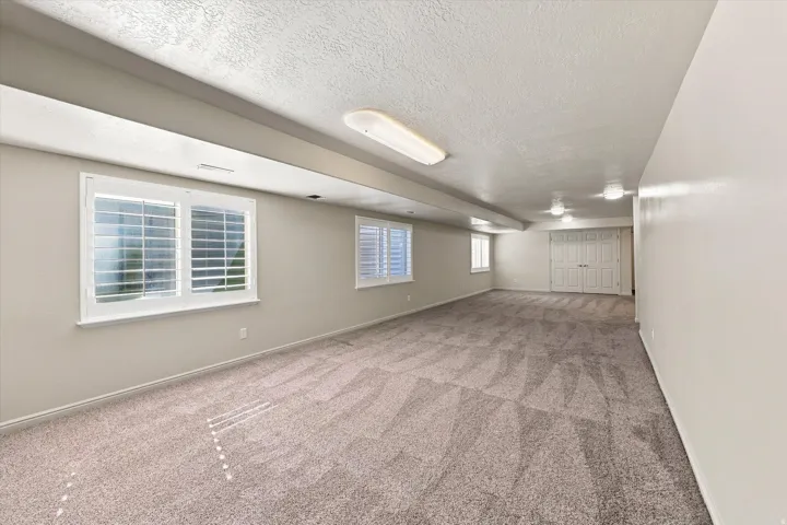Spacious room with patterned carpet flooring, multiple windows featuring plantation shutters, and recessed lighting