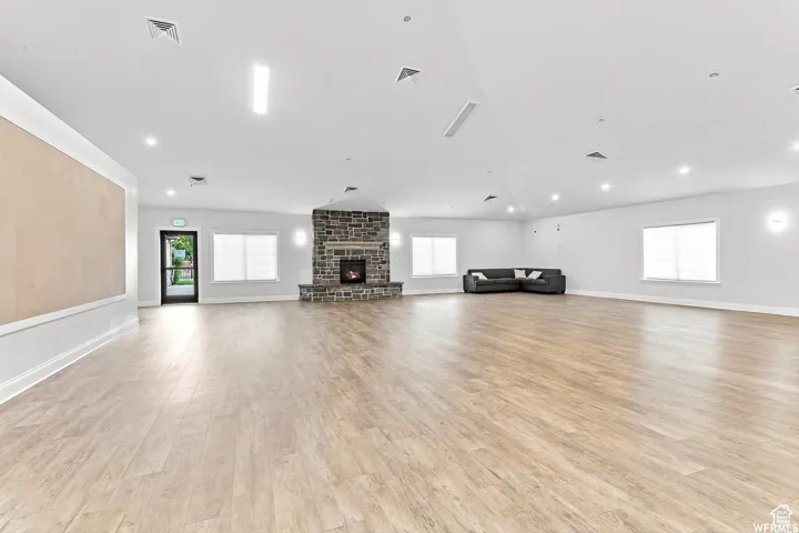 Spacious room featuring wood-finish flooring, a stone fireplace, recessed lighting, multiple windows, and a built-in wall panel