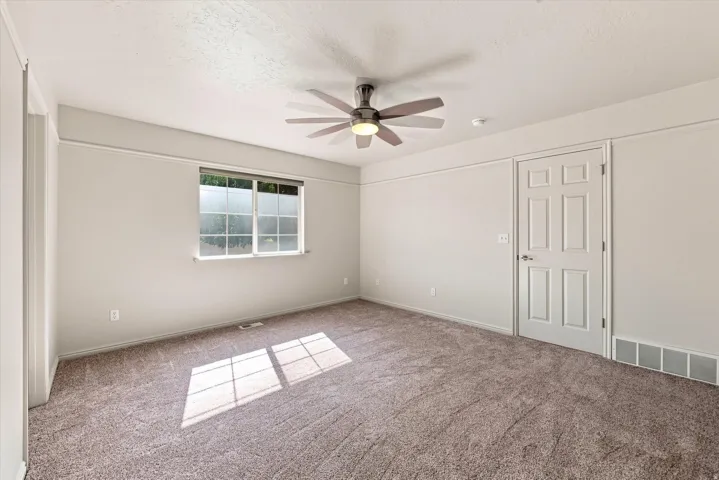 Neutral wall paint, textured carpet flooring, ceiling fan with integrated lighting, white trim work, and a six-panel interior door