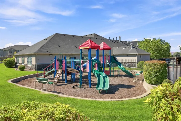Recreational playground structure with multiple slides and climbing features, surrounded by woodchip surfacing and a retaining wall