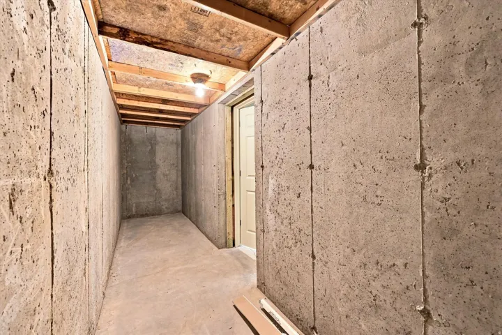 Unfinished concrete walls, unfinished concrete flooring, exposed wood ceiling joists, and a flush-mounted light fixture
