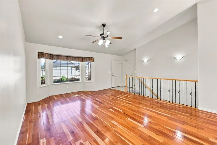 Hardwood flooring, bay window, vaulted ceiling, ceiling fan, and wrought iron railing